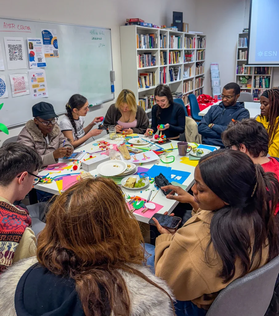 A diverse group of university students engaged in arts and crafts around tables, focusing on colorful paper and materials, fostering a lively and creative atmosphere.